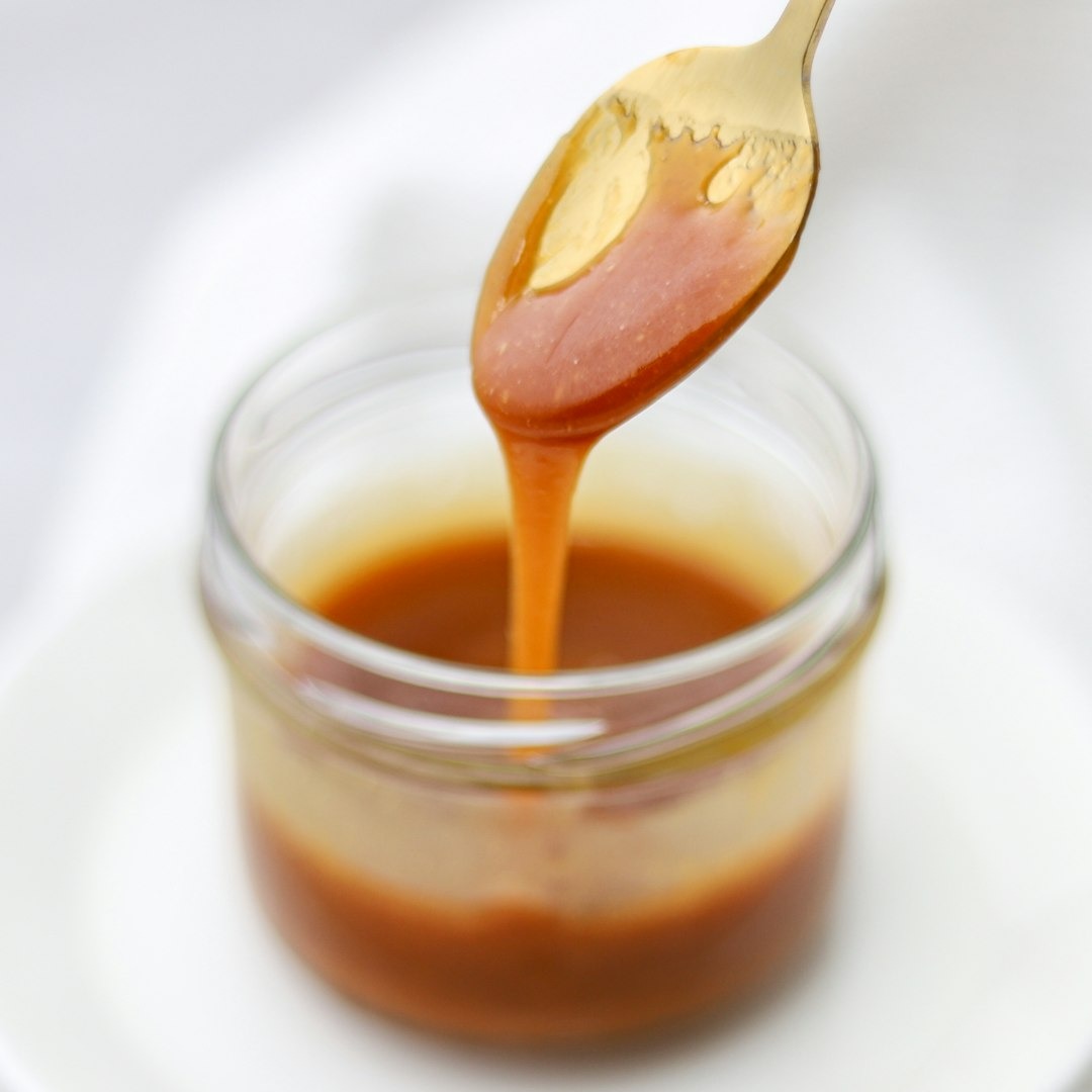 Salted caramel running off a gold spoon into a glass jar